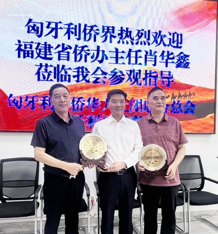 匈华总会主席，匈牙利中国统促会会长余美明（左）；匈华总会执行主席、匈牙利福建商会会长刘文建（右）囎送给福建省侨办主任肖华鑫（中）会徽纪念品